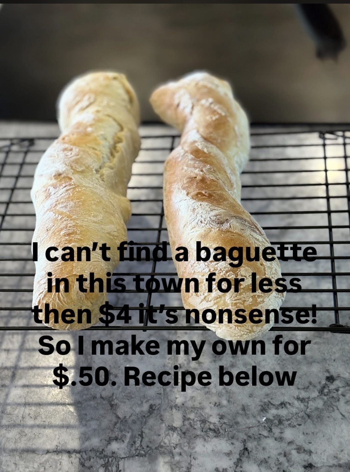 Two freshly baked golden-brown French baguettes cooling on a wire rack over a countertop.
